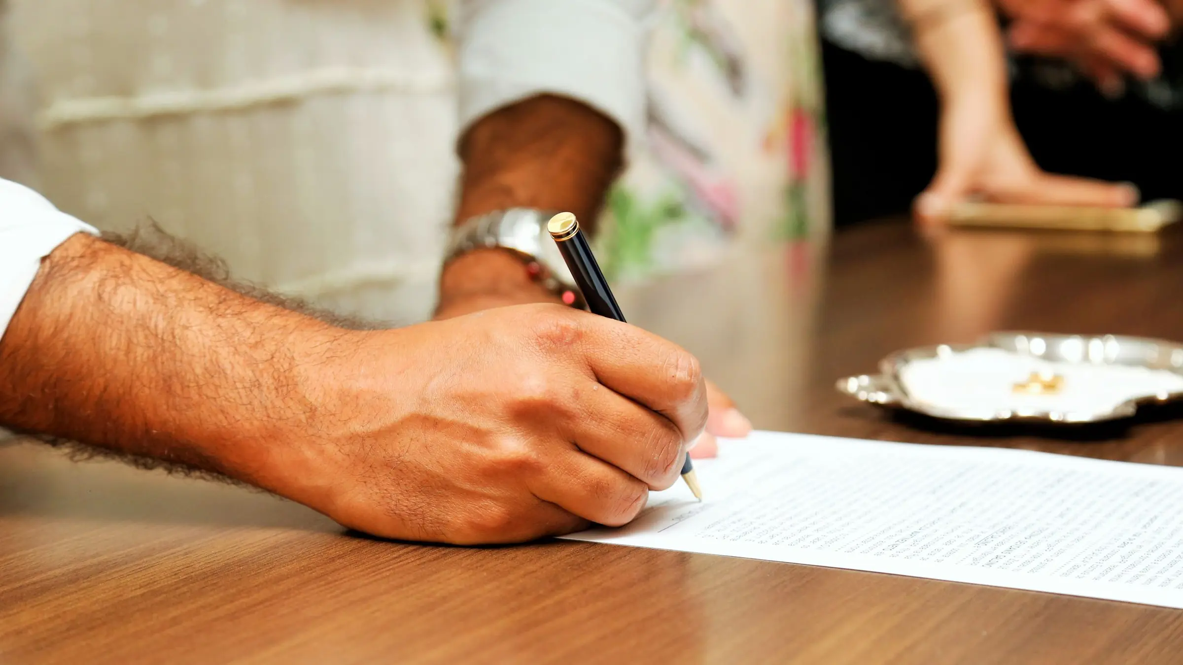 Manos firmando un documento con bolígrafo sobre una mesa de madera